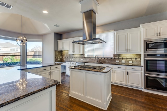 kitchen featuring appliances with stainless steel finishes, island range hood, white cabinetry, dark stone counters, and a center island