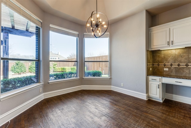 unfurnished dining area featuring dark wood-type flooring, built in desk, and a chandelier