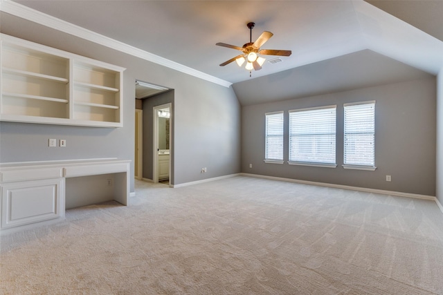 unfurnished living room with lofted ceiling, built in desk, light colored carpet, ornamental molding, and ceiling fan