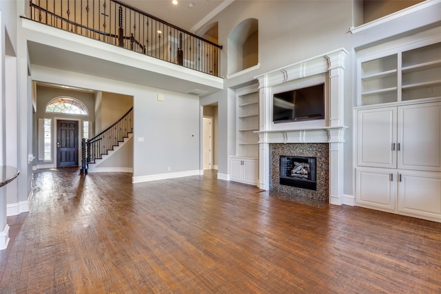 unfurnished living room with a high ceiling, dark wood-type flooring, a fireplace, and built in shelves