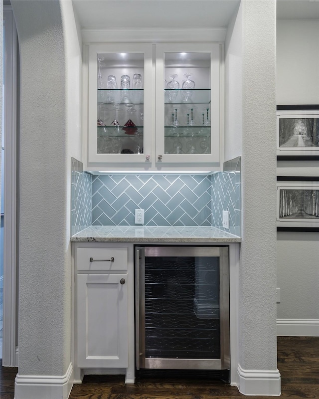 bar with wine cooler, white cabinetry, light stone countertops, and tasteful backsplash