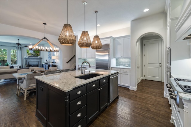 kitchen featuring pendant lighting, sink, white cabinetry, built in appliances, and a center island with sink