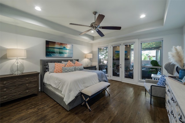 bedroom featuring access to exterior, a tray ceiling, dark wood-type flooring, and ceiling fan