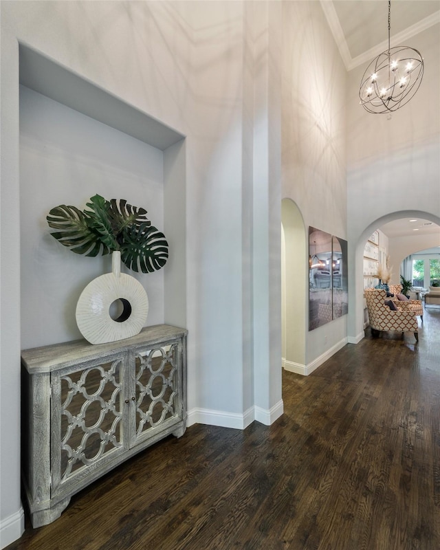 hallway with crown molding, dark wood-type flooring, a chandelier, and a high ceiling