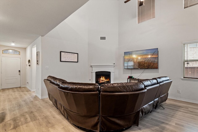 living room with a high ceiling, ceiling fan, and light wood-type flooring