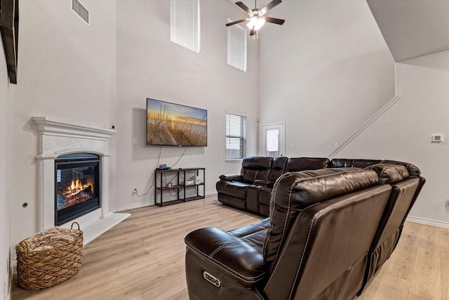 living room with a towering ceiling, ceiling fan, and light hardwood / wood-style flooring