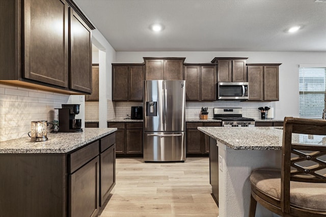 kitchen featuring light stone counters, dark brown cabinetry, and appliances with stainless steel finishes