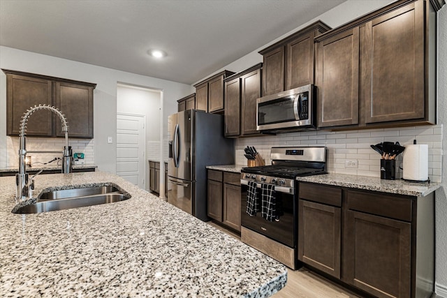 kitchen with stainless steel appliances, light stone countertops, sink, and dark brown cabinets