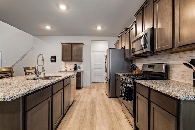 kitchen featuring light stone counters, sink, stainless steel appliances, and light wood-type flooring