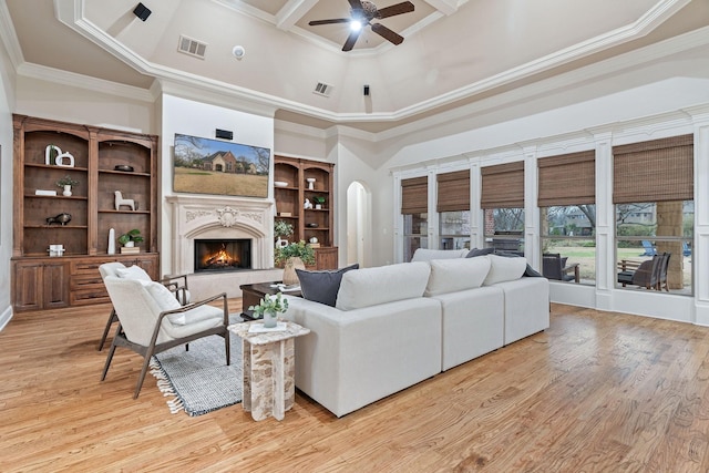 living room with a high ceiling, crown molding, light wood-type flooring, and a fireplace