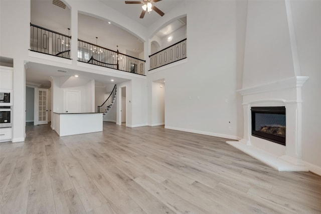 unfurnished living room featuring ceiling fan, a towering ceiling, and light wood-type flooring