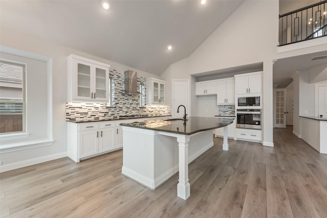 kitchen with white cabinetry, sink, stainless steel appliances, a center island with sink, and wall chimney exhaust hood