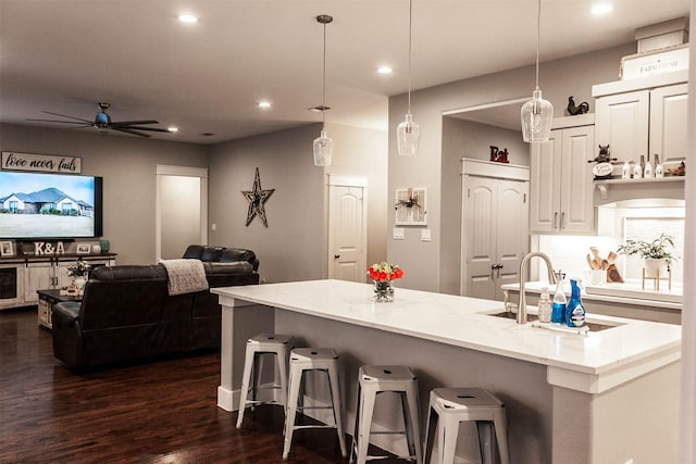 kitchen featuring dark wood-type flooring, white cabinetry, light stone counters, a ceiling fan, and decorative light fixtures