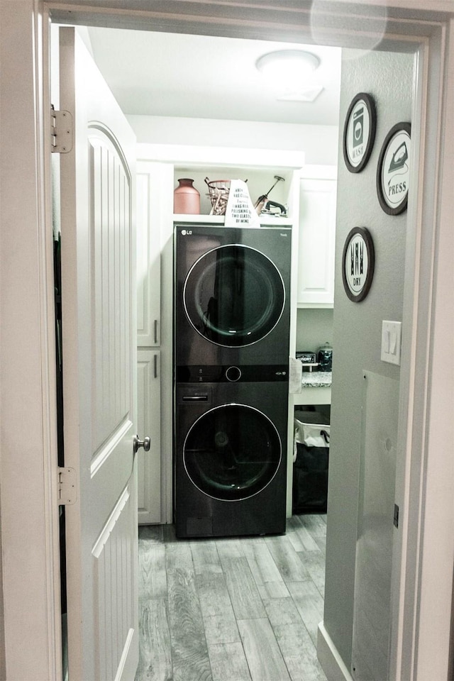 laundry area featuring light wood-type flooring, stacked washer and dryer, and cabinet space