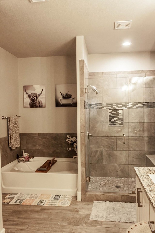bathroom with vanity, visible vents, wood finished floors, a bath, and a shower stall