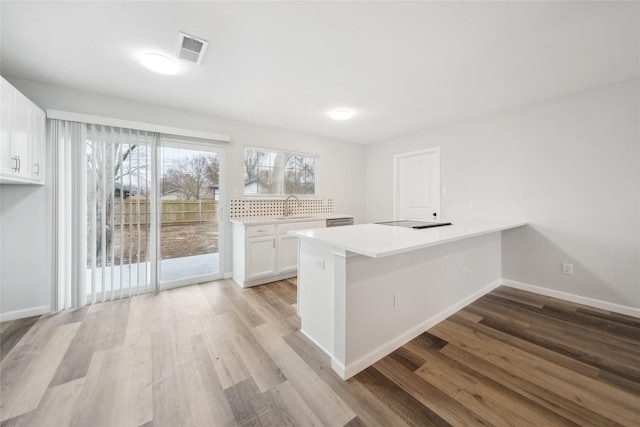 kitchen with sink, kitchen peninsula, white cabinets, cooktop, and light wood-type flooring