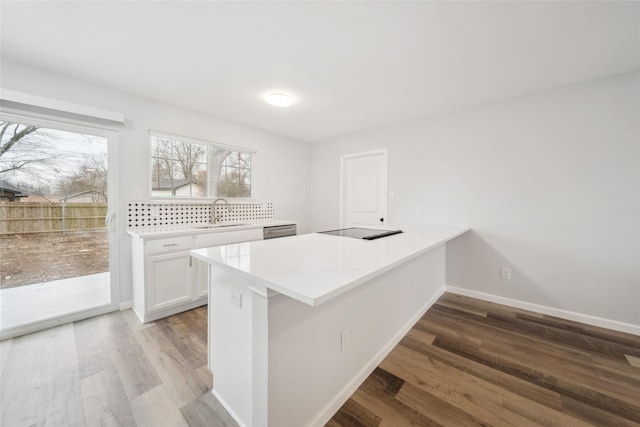 kitchen featuring sink, black electric cooktop, kitchen peninsula, light hardwood / wood-style floors, and white cabinets