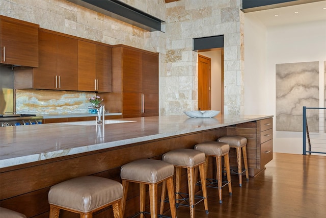 kitchen featuring a breakfast bar, stove, tasteful backsplash, light stone countertops, and dark hardwood / wood-style flooring