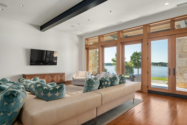 living room with a water view, beamed ceiling, and light wood-type flooring