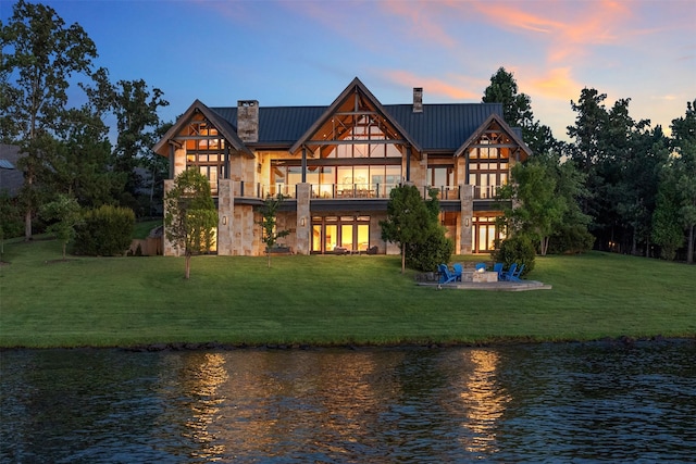 back house at dusk featuring a patio area, a lawn, a balcony, and a water view