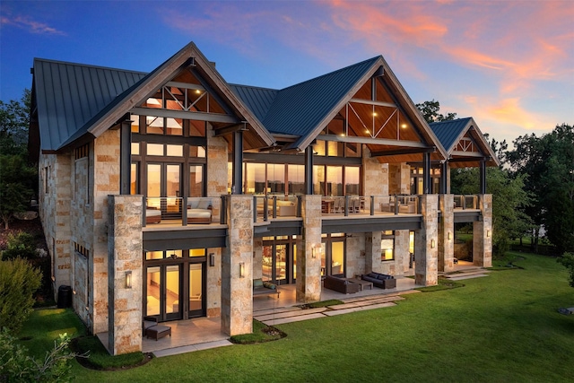 back house at dusk with a yard, a patio, and a balcony