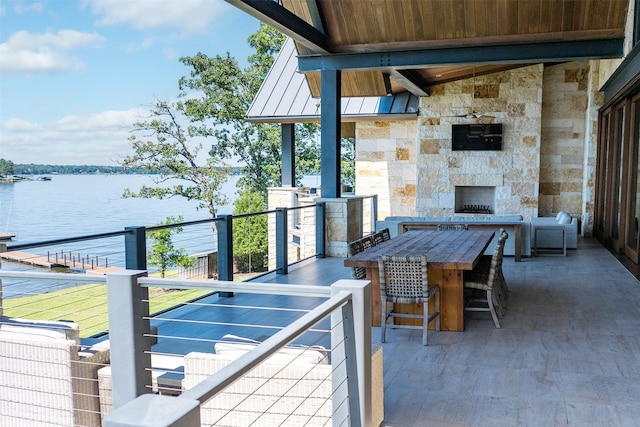 view of patio featuring a water view, a bar, and an outdoor stone fireplace