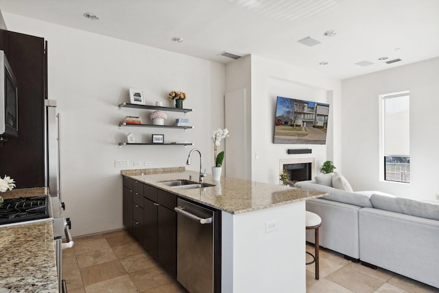 kitchen featuring sink, kitchen peninsula, stainless steel appliances, light stone countertops, and dark brown cabinets