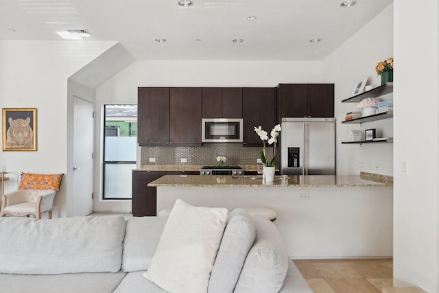 kitchen featuring stainless steel appliances, light stone countertops, backsplash, and dark brown cabinetry