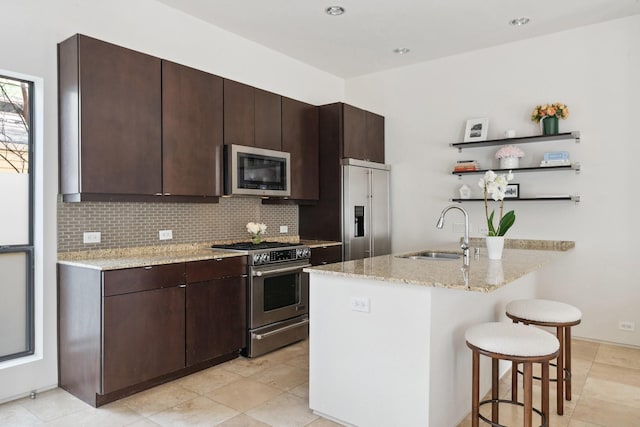 kitchen featuring dark brown cabinetry, sink, light stone counters, appliances with stainless steel finishes, and decorative backsplash