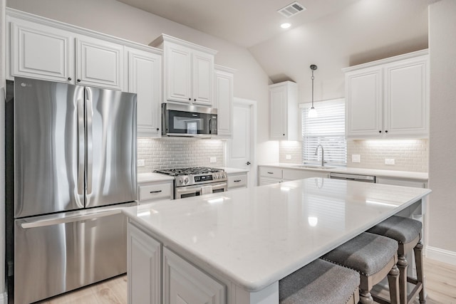 kitchen with lofted ceiling, a sink, visible vents, white cabinets, and appliances with stainless steel finishes