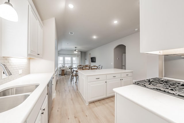 kitchen with light wood finished floors, arched walkways, a ceiling fan, open floor plan, and a sink