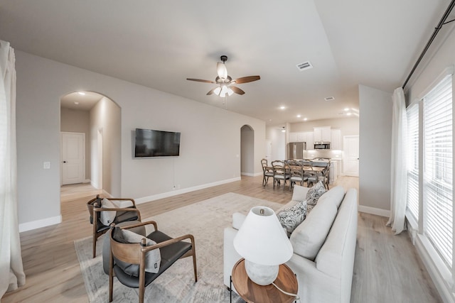 living area featuring light wood-style floors, visible vents, arched walkways, and ceiling fan