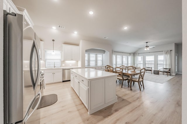 kitchen featuring visible vents, arched walkways, appliances with stainless steel finishes, a center island, and white cabinetry