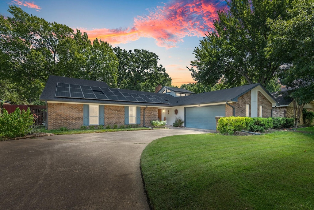 ranch-style home featuring a garage, a lawn, and solar panels