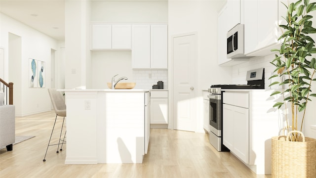 kitchen with a breakfast bar area, gas range, white cabinetry, a center island with sink, and light wood-type flooring