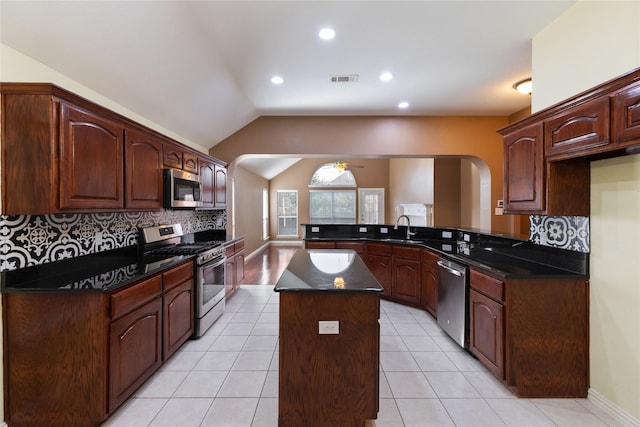 kitchen featuring appliances with stainless steel finishes, tasteful backsplash, a kitchen island, vaulted ceiling, and kitchen peninsula