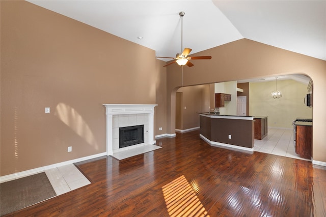 unfurnished living room featuring vaulted ceiling, hardwood / wood-style floors, ceiling fan with notable chandelier, sink, and a tiled fireplace