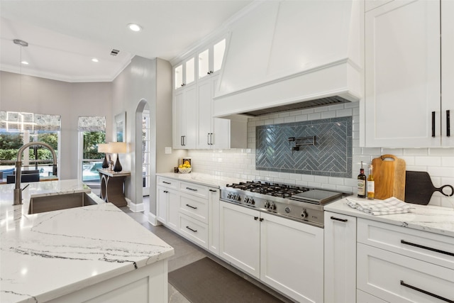 kitchen with sink, stainless steel gas cooktop, white cabinetry, decorative light fixtures, and light stone countertops