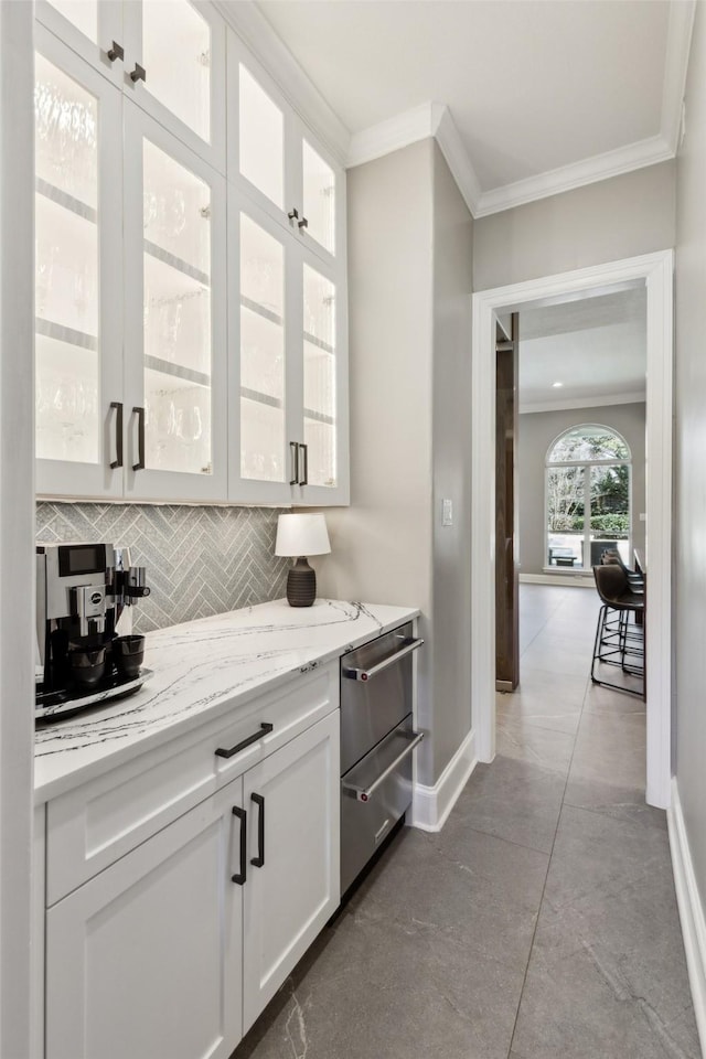 bar with tasteful backsplash, crown molding, light stone countertops, and white cabinets