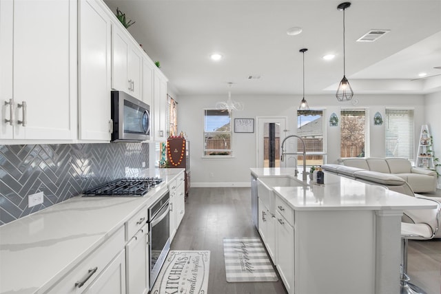 kitchen featuring tasteful backsplash, stainless steel appliances, hanging light fixtures, and white cabinets