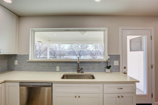 kitchen featuring light countertops, backsplash, stainless steel dishwasher, white cabinetry, and a sink