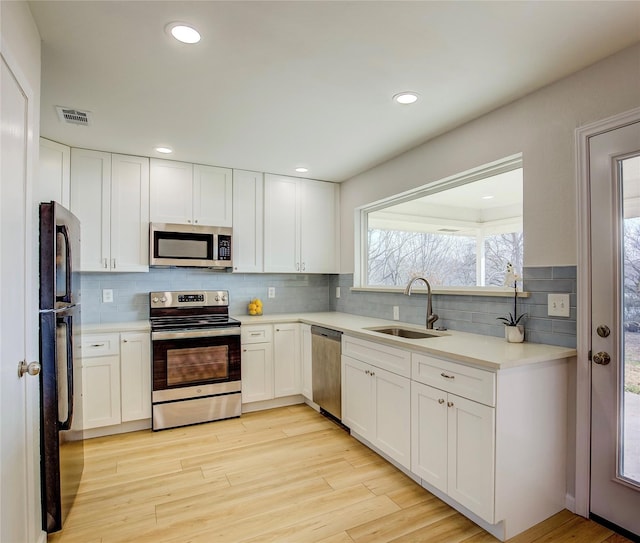 kitchen featuring stainless steel appliances, visible vents, backsplash, a sink, and light wood-type flooring