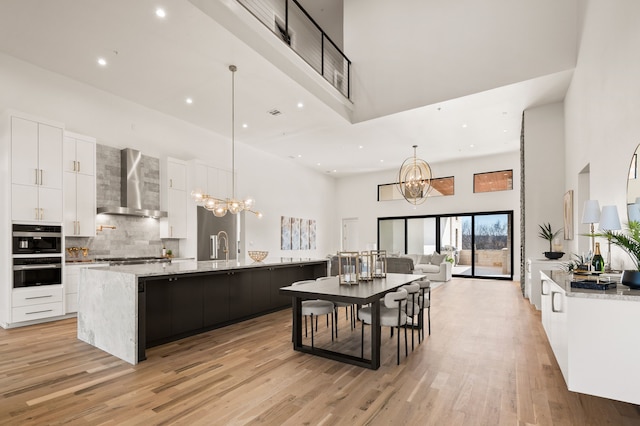 kitchen featuring wall chimney exhaust hood, a high ceiling, light wood-style floors, and a notable chandelier