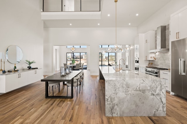 kitchen featuring wall chimney exhaust hood, high end refrigerator, decorative light fixtures, a chandelier, and white cabinets