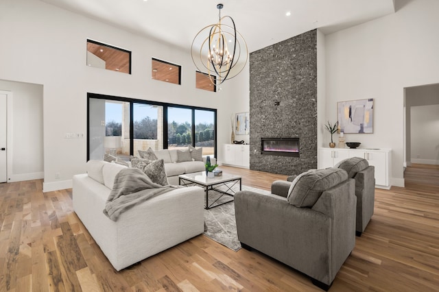 living room featuring a towering ceiling, a large fireplace, a notable chandelier, and light hardwood / wood-style flooring