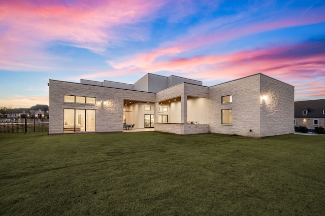 back house at dusk featuring a lawn and a patio area