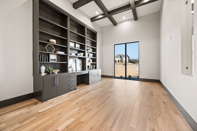 interior space featuring built in desk, a high ceiling, coffered ceiling, light hardwood / wood-style floors, and beam ceiling