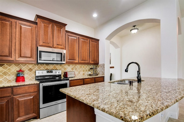 kitchen featuring a kitchen island with sink, sink, light stone countertops, and appliances with stainless steel finishes