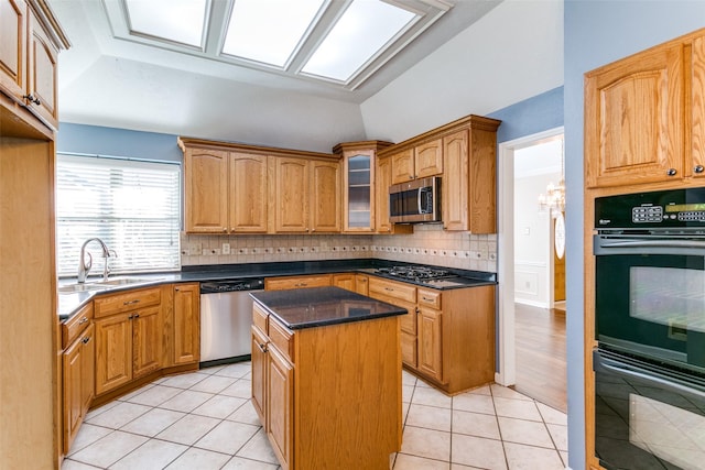 kitchen with light tile patterned floors, sink, appliances with stainless steel finishes, vaulted ceiling with skylight, and a kitchen island