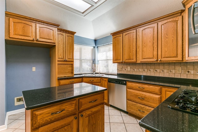 kitchen with vaulted ceiling with skylight, dishwasher, backsplash, a center island, and light tile patterned floors